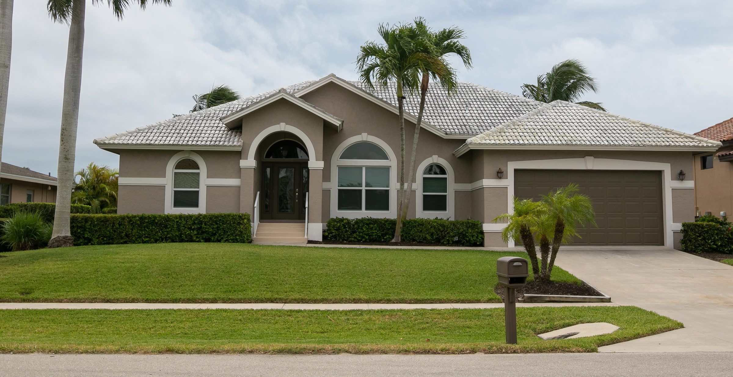 A stucco house with a tile roof, a lawn and a palm tree